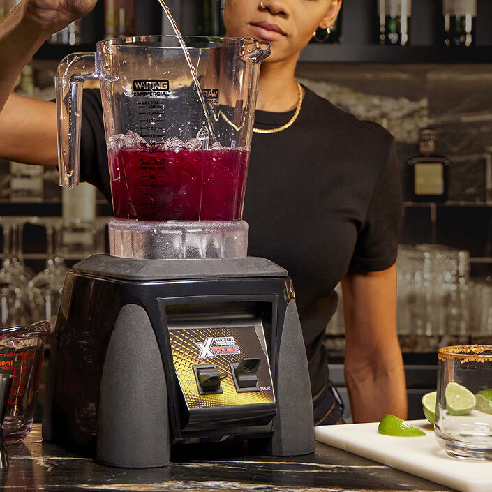 bartender pouring ingredients into blender on bar